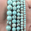 A string of light blue turquoise beads with natural marbling are held in a hand.