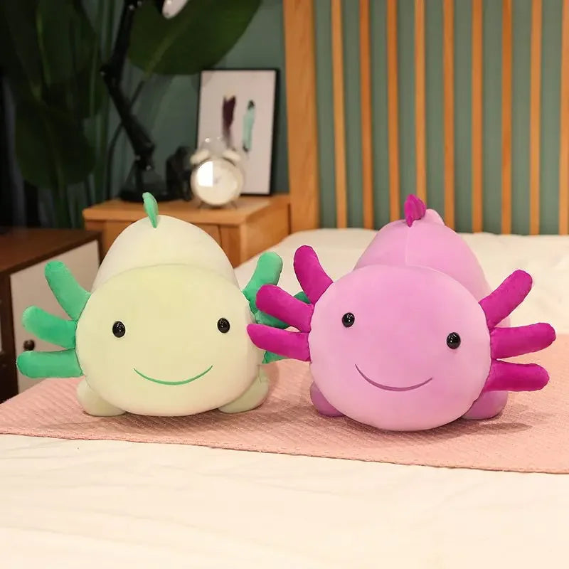 Two soft plush axolotl pillows, one light green and one pink, resting on a white surface.