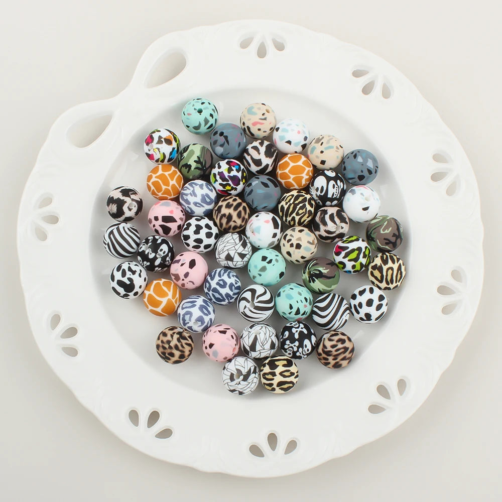 A collection of 30 small, round silicone beads in leopard print and daisy patterns arranged on a white dish.