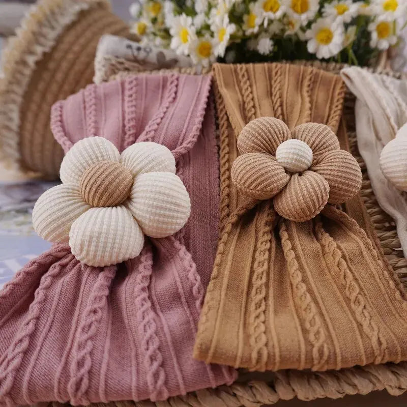A collection of knitted floral elastic baby headbands in pink and beige tones.