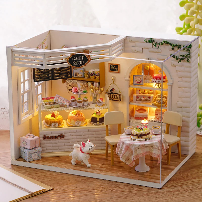 A miniature dollhouse kit featuring a white brick facade, furniture, and a small white kitten figure.