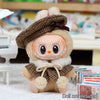A fluffy doll wearing a brown tweed beret and cape set with a stitched smile.
