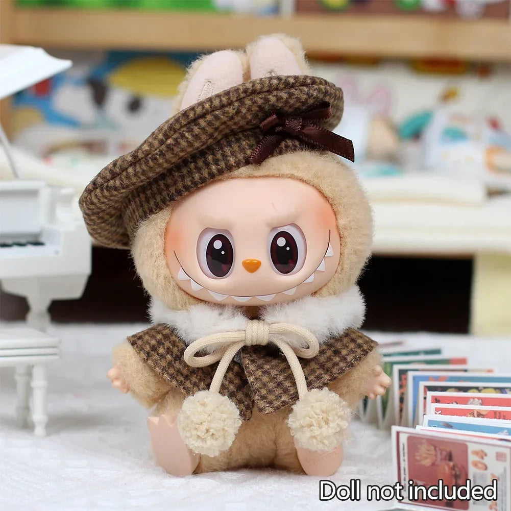 A fluffy doll wearing a brown tweed beret and cape set with a stitched smile.
