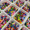 A collection of colorful acrylic letter beads in various shades and shapes arranged in small white plastic containers.
