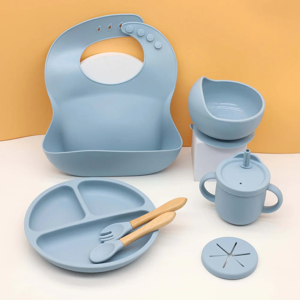 A light blue silicone baby tableware set featuring a feeding bowl, plate, spoon, and other accessories.