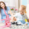 A pink multi-size button making machine kit is shown with a baby and an adult in a bright indoor setting.