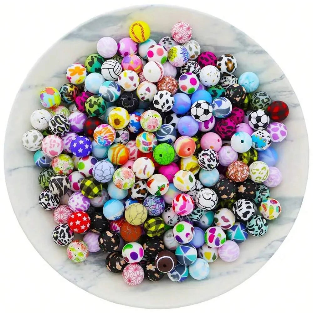 A colorful assortment of 15mm printed silicone beads for DIY jewelry making scattered on a white marble plate.