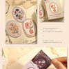 A hand holds a sheet of vintage floral stickers for scrapbooking and journaling on a light-colored background.