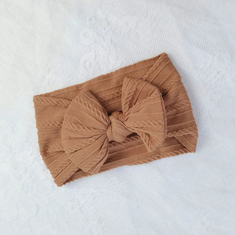 A brown knitted baby headband with a large bow shown on a white background.