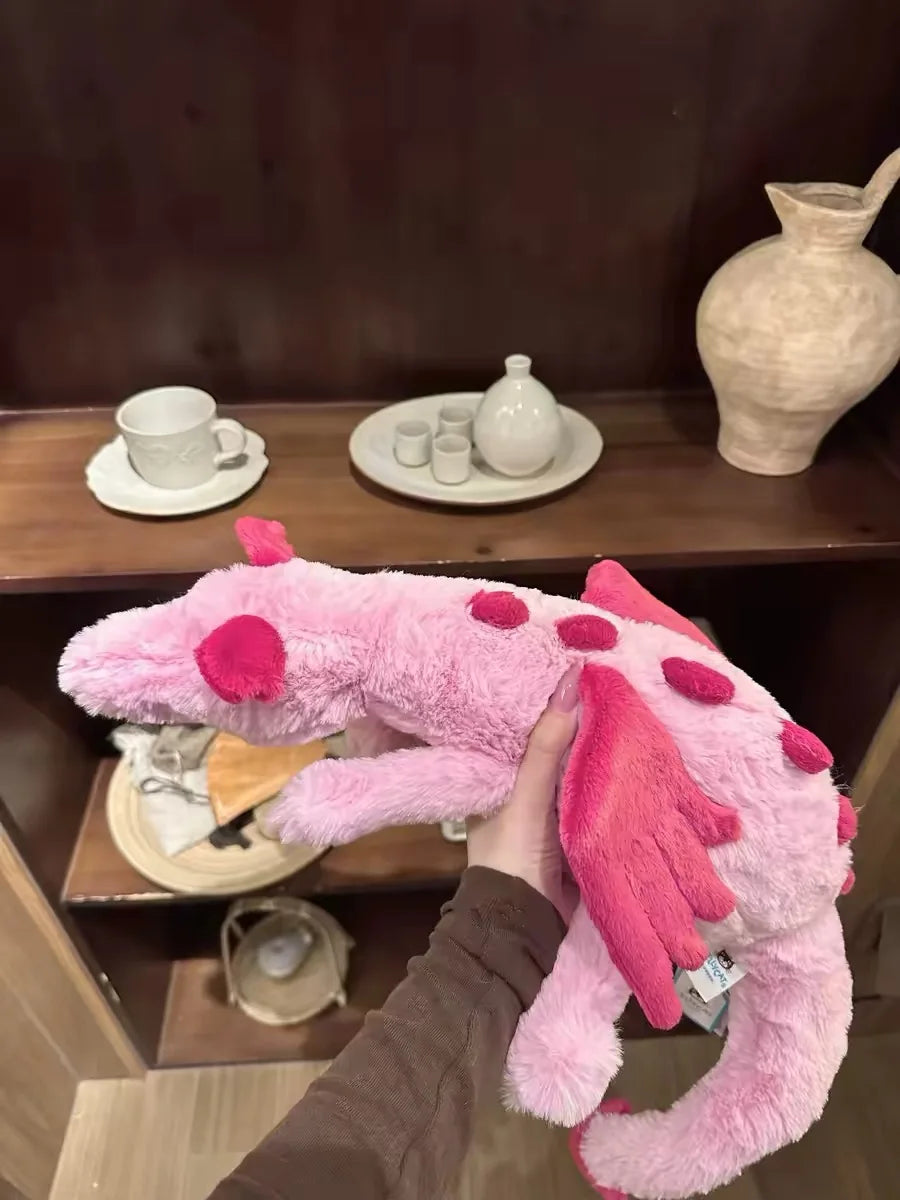 A person is holding a pink rainbow dragon plush toy, showcasing its soft texture and features.