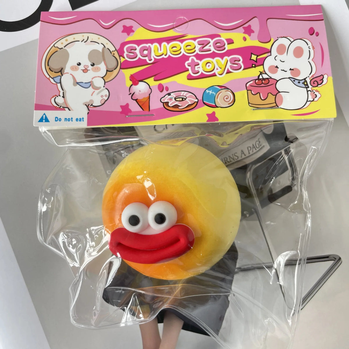 A yellow squishy toy shaped like a smiling face is packaged in a pink box labeled squeeze toys.
