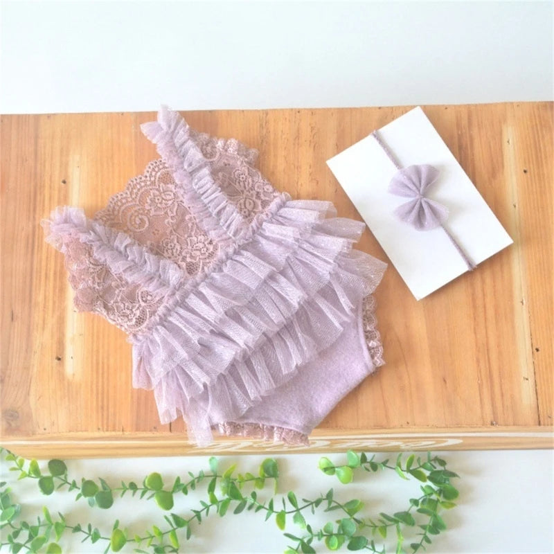 A light pink lace baby romper with ruffled tiers and a matching lavender headband displayed on a wooden surface.