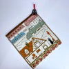 A handmade embroidered quilt featuring a scene with buildings, trees, and a black cat.
