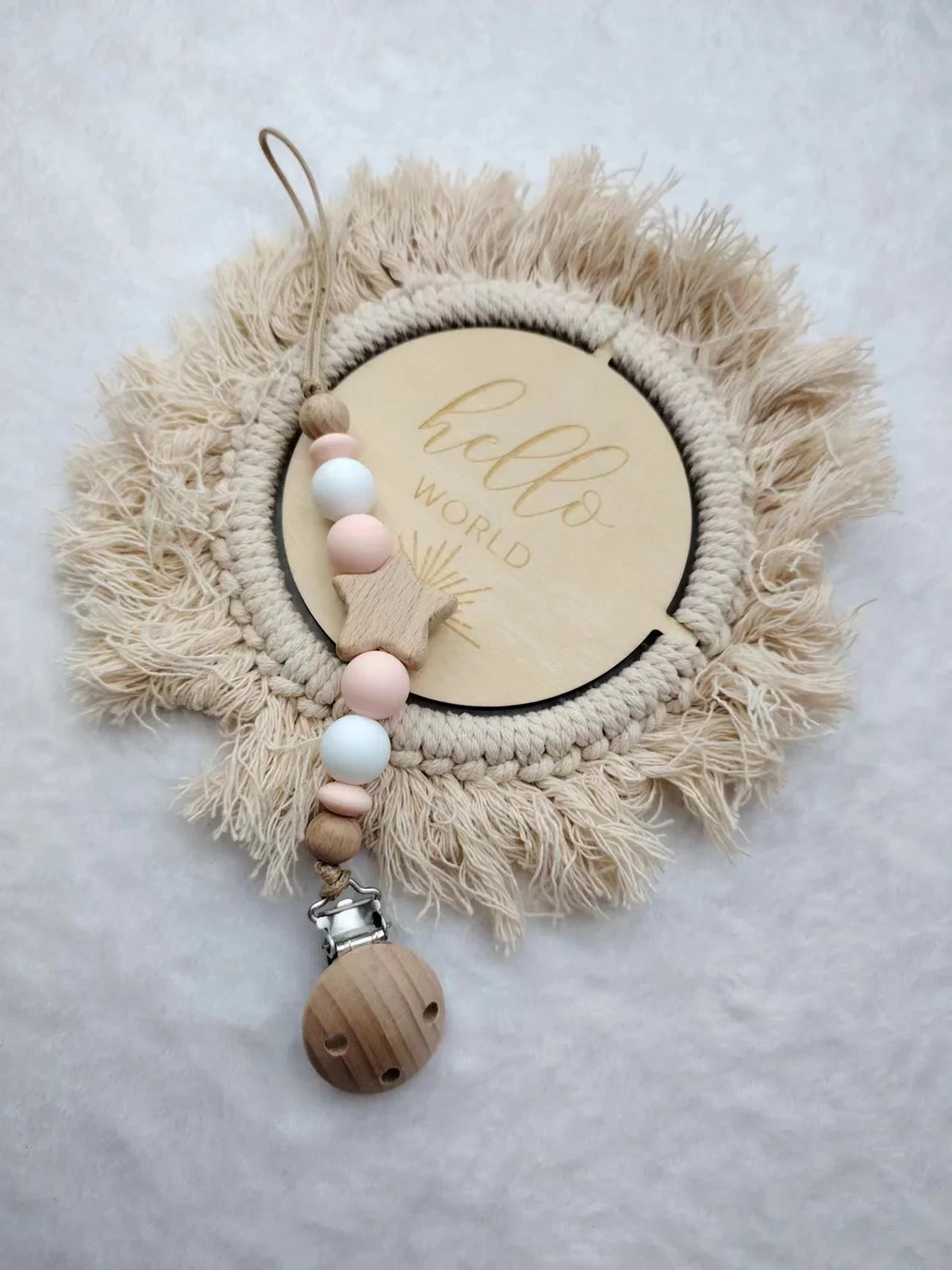 A personalized wooden baby pacifier clip featuring silicone beads and a natural fiber wreath with the word hello world.