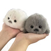 A pair of adorable grey seal plush keychains, one white and one grey, held in a person's hand.