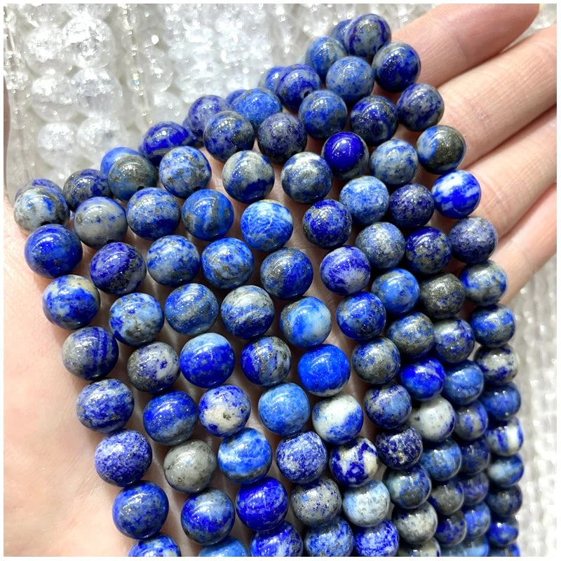 A hand holds a strand of deep blue and gray natural stone beads for DIY jewelry making.