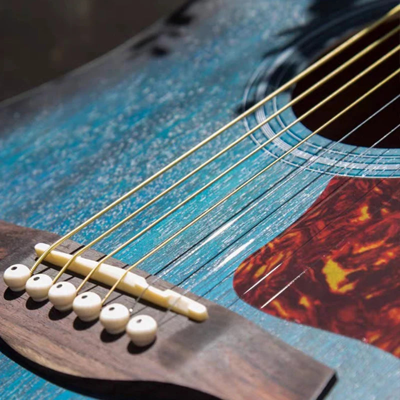 Close-up of a blue acoustic guitar with golden strings and a wooden string changer tool.