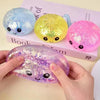 Three squishy glitter steamed bun fidget toys in blue, yellow, and pink are displayed on a book.