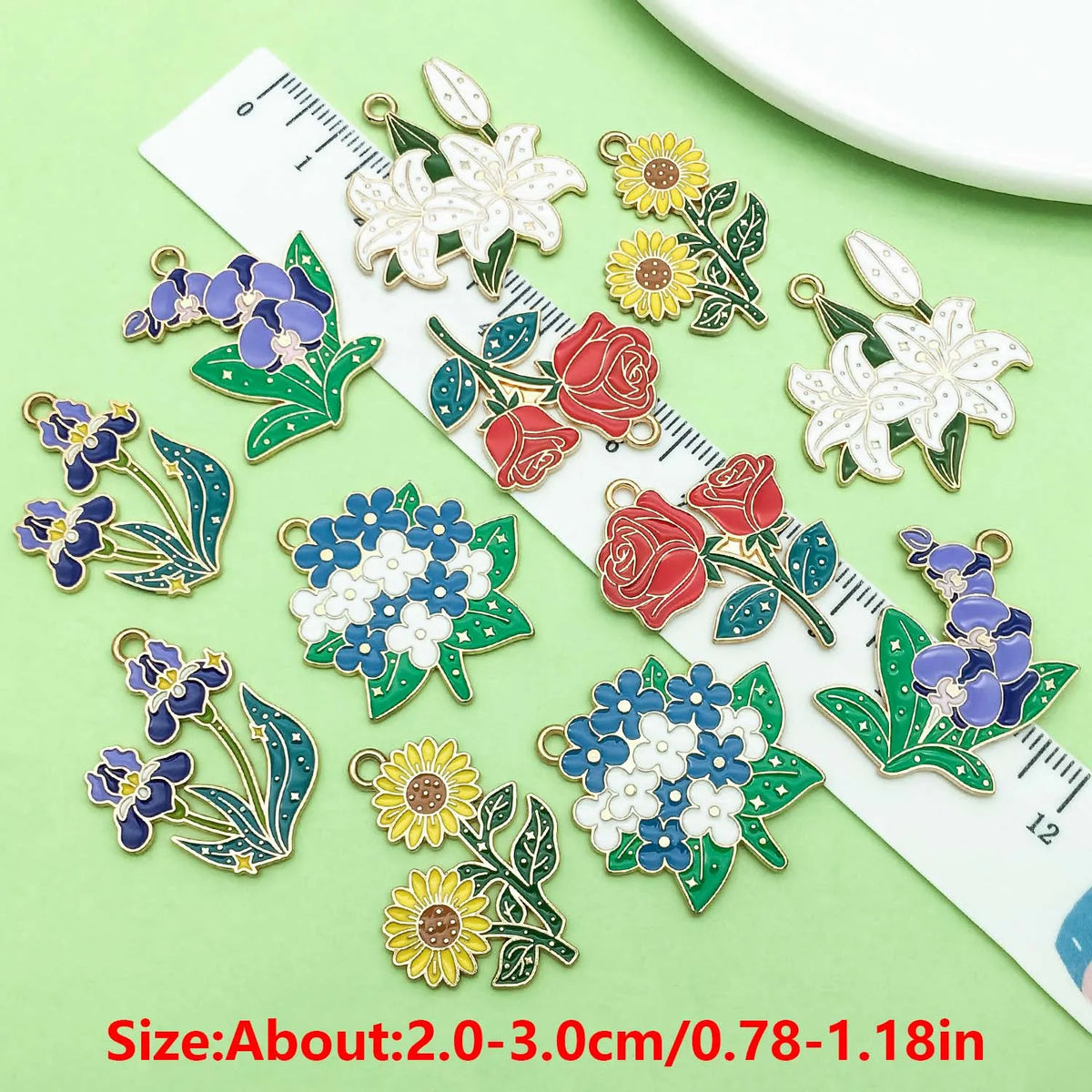 A collection of colorful enamel flower charms displayed on a ruler for size reference.