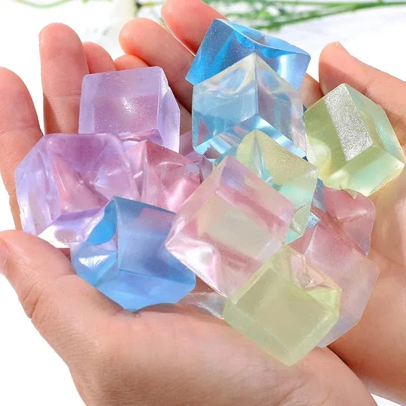 A hand holds several translucent, geometric ice cube squishy fidget toys in shades of blue, pink, and green.