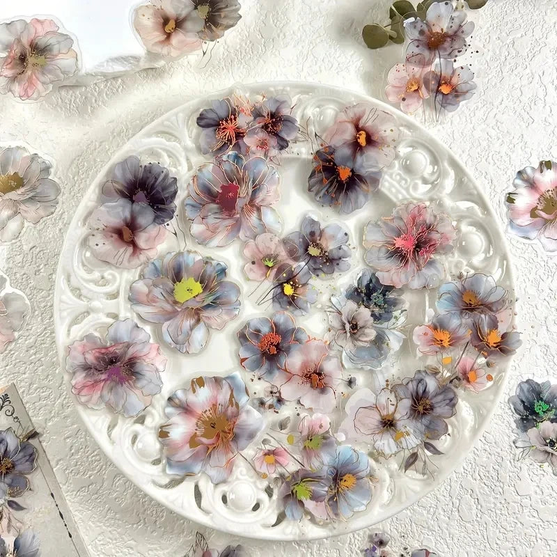 A white plate filled with pressed floral hot stamp stickers in shades of purple, pink, and gray.