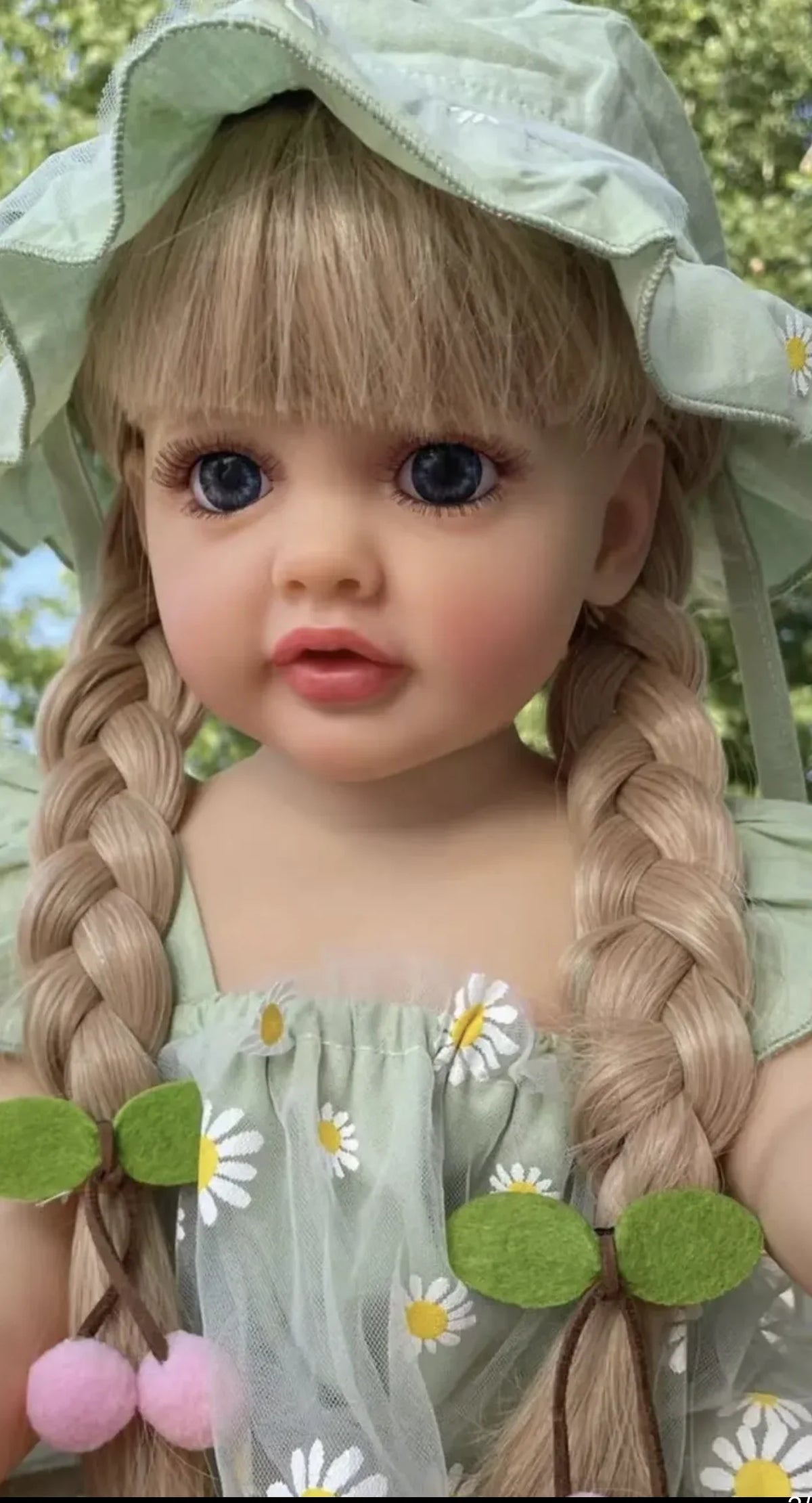 A realistic silicone vinyl toddler doll named Betty with light brown hair styled in braids and wearing a green sheer dress.