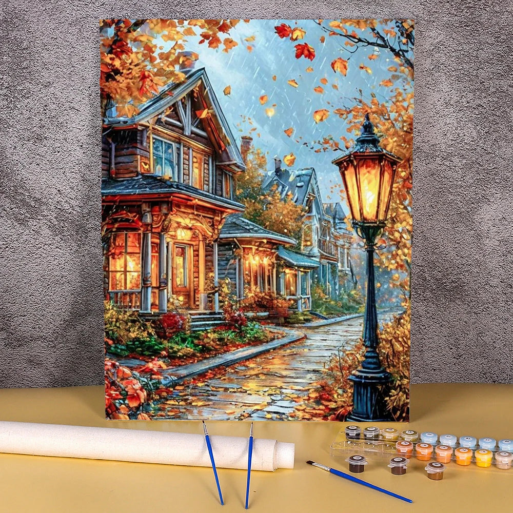 A paint by numbers kit depicting a detailed landscape of a wooden house and flower field during autumn.