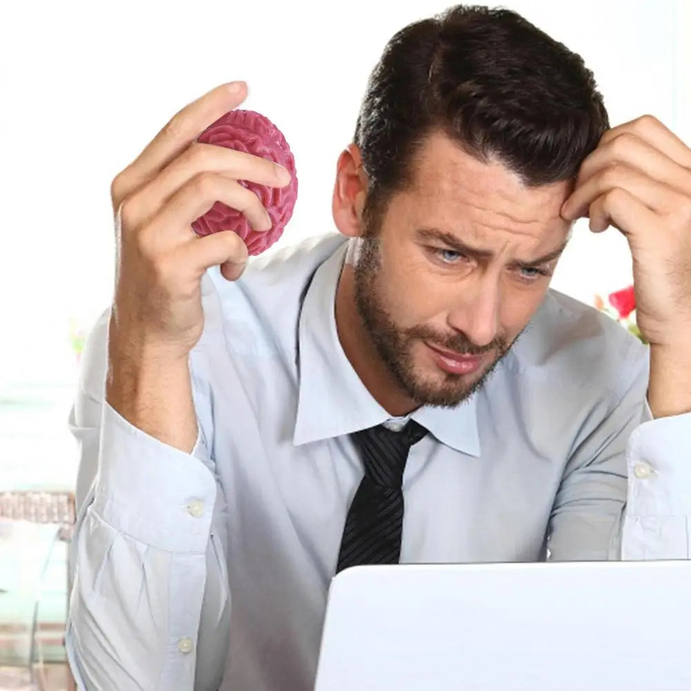 A man holds a pink brain-shaped stress relief ball while looking stressed near a laptop.