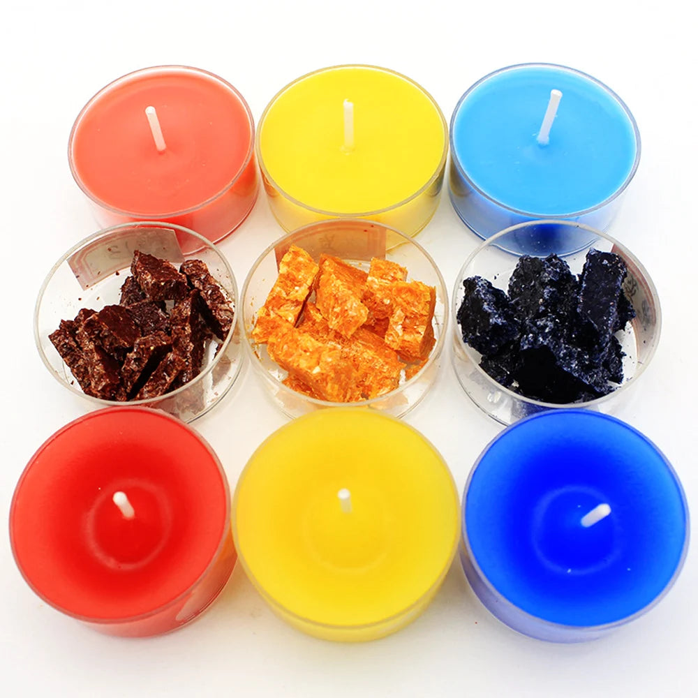 A collection of six colored candle dye chips in red, yellow, blue, and black displayed in glass containers.
