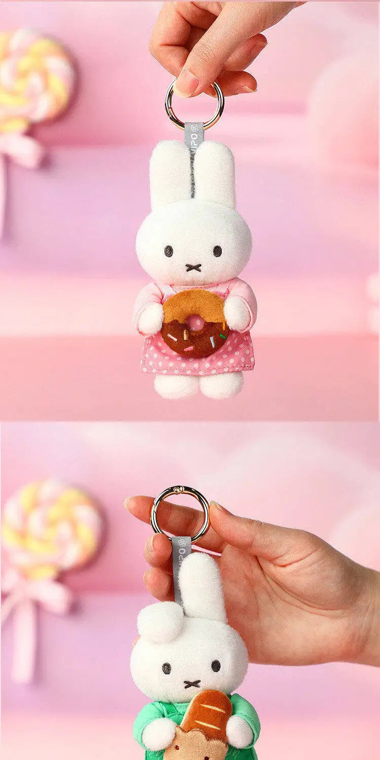 A white Miffy plush keychain charm with a pink dress and an orange donut, being held by a hand.