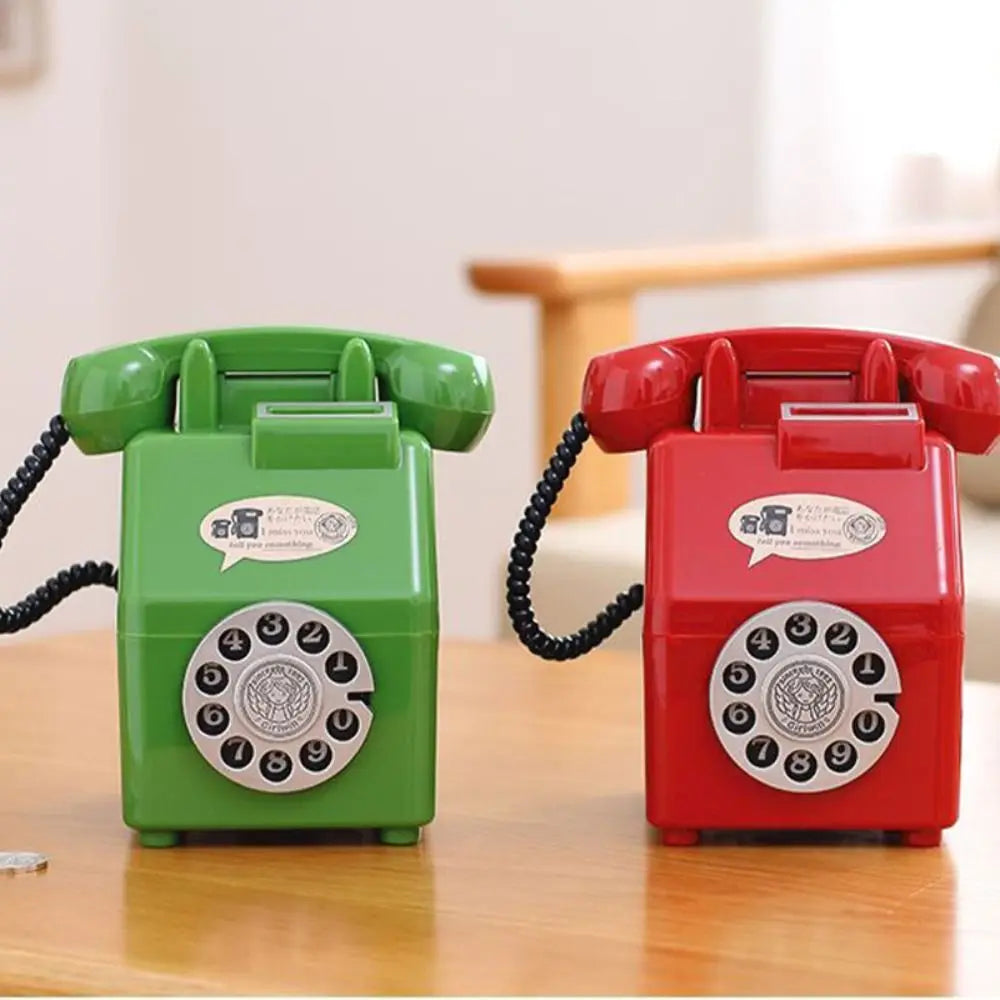 A pair of vintage rotary telephone piggy banks, one green and one red, sitting on a wooden surface.