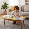 A young boy is crafting with a colorful geometric animal sticker book on a wooden table indoors.