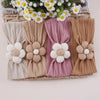 A set of four floral elastic baby headbands in cream, beige, pink, and tan are displayed in a woven basket.