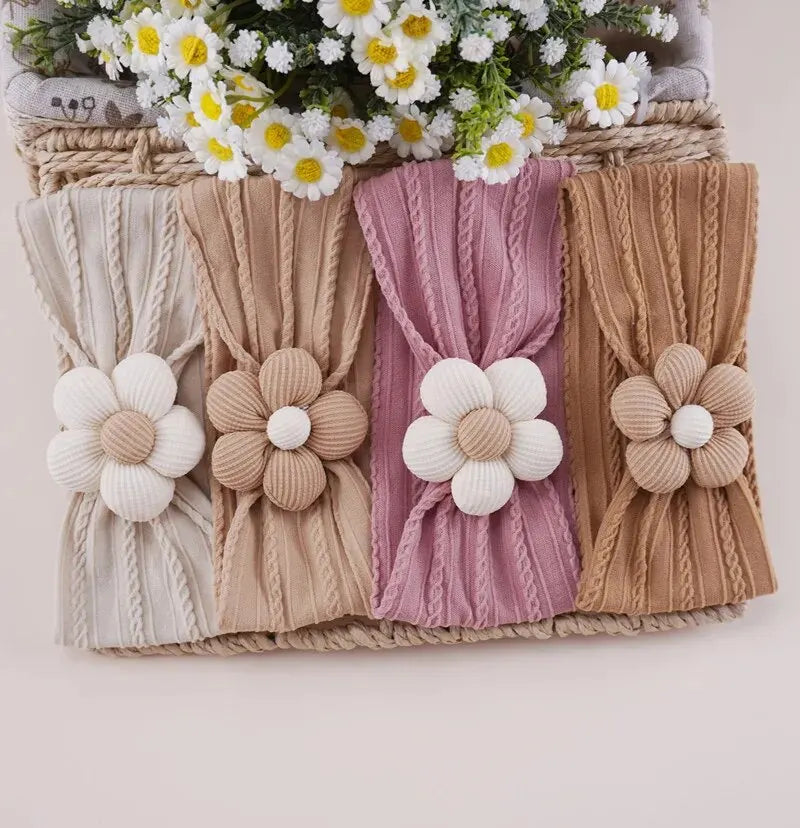 A set of four floral elastic baby headbands in cream, beige, pink, and tan are displayed in a woven basket.