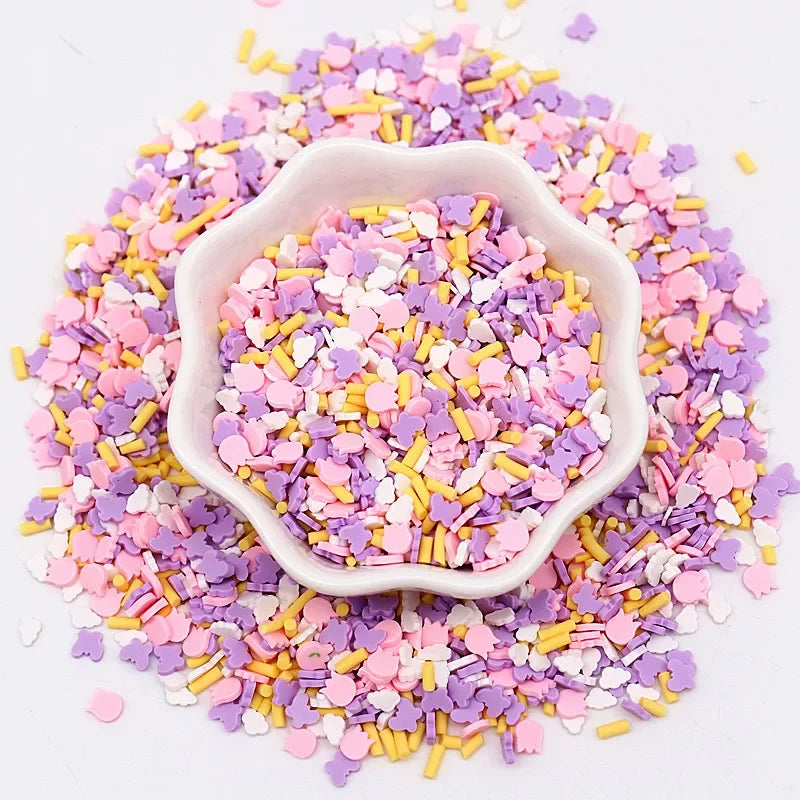 A pile of pink, purple, and yellow polymer clay sprinkles on a white surface, with a small pink dish in the center.