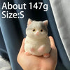 A small, white cat-shaped squishy toy is held in a person's hand against a dark blue fabric background.