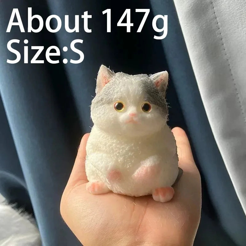 A small, white cat-shaped squishy toy is held in a person's hand against a dark blue fabric background.