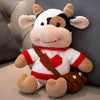 A soft stuffed animal of a cow with white and black markings, wearing a red collar and brown harness.