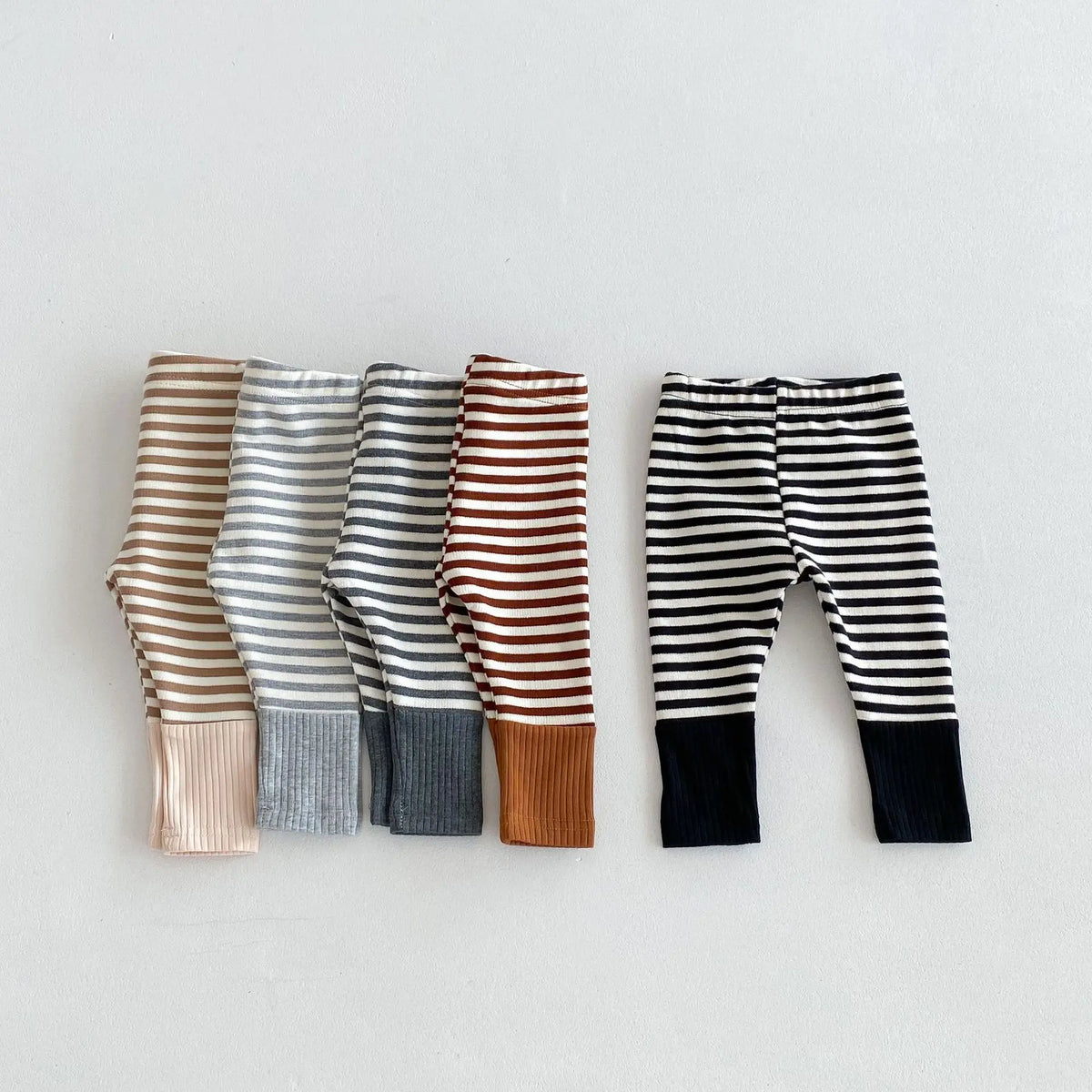 A collection of soft cotton baby leggings featuring various striped designs in brown, gray, and black.