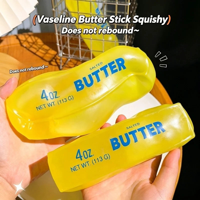 A hand holds a yellow silicone butter stick squishy toy labeled 4oz butter with a salted scent.
