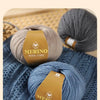 A close-up of a ball of grey merino wool yarn resting on a blue knitted fabric.