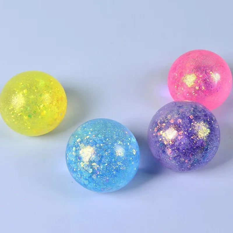 Three spherical glitter balls in yellow, pink, and blue are displayed on a white surface.