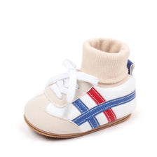 A pair of beige baby booties with white laces and blue and red stripes on the side.