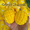 A hand holds a bright yellow mango squishy stress relief ball with a crispy texture.