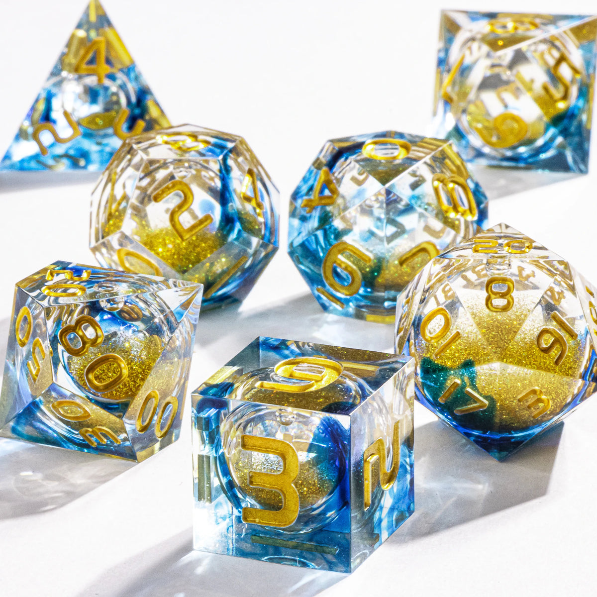 A collection of blue and gold polyhedral dice with a galaxy finish scattered on a white surface.