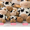 A collection of soft plush cow stuffed animals in black and white patterns displayed on a light surface.
