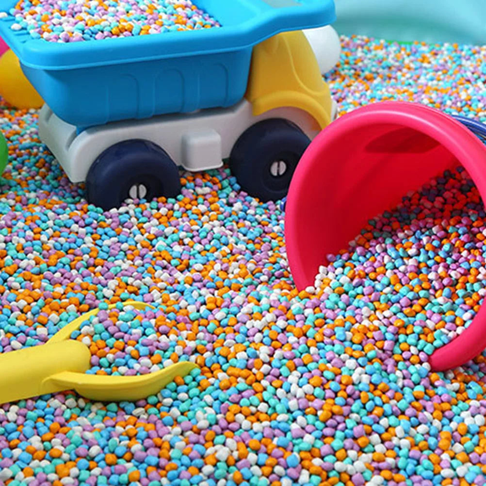 A yellow and blue toy vehicle is placed on a colorful sensory play surface covered with multicolored plastic beads.