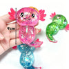 A hand holds a pink glitter axolotl squishy stress relief toy with a 9cm scale marker.