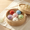 A set of adorable squishy dumpling keychain plush toys in various pastel colors resting in a wooden tray.