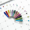 A collection of thirteen colorful DIY beaded ballpoint pen craft needles and tips arranged on a white grid.